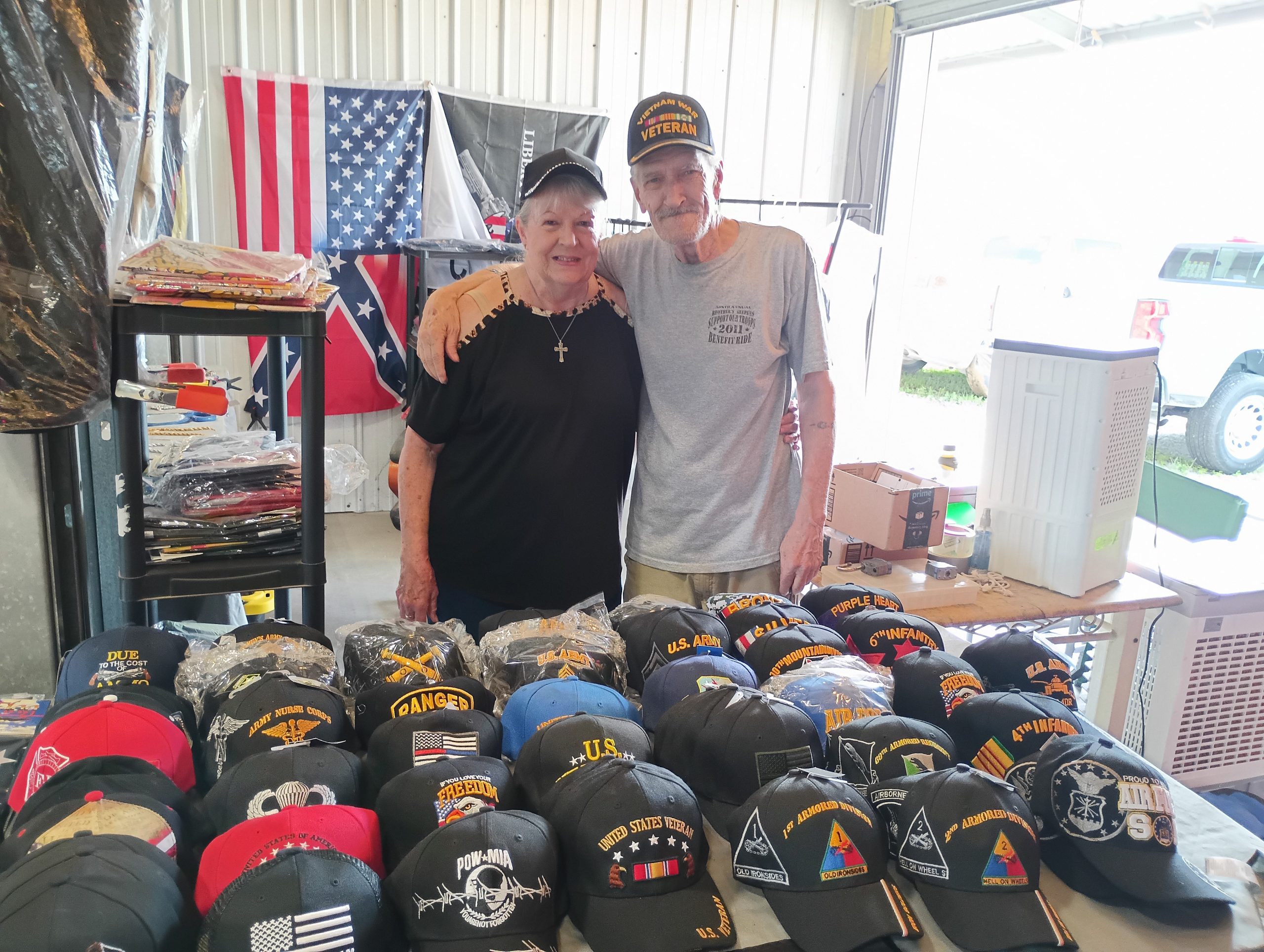 Jerry and Dolores Colwart at Booth 230 - August 2025 Vendor of the Month at Lafayette Jockey Lot, featuring military caps, sports jerseys, and jewelry
